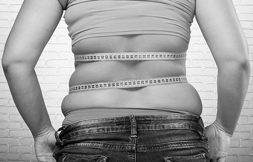 Back of woman with measuring tape around her body to illustrate weight loss